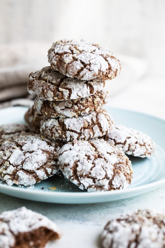 Hazelnut crinkle cookies feature plenty of chocolate-hazelnut spread and crunchy hazelnuts. A delicious twist on chocolate crinkle cookies! Hazelnut crinkle cookies stacked on a light blue plate.