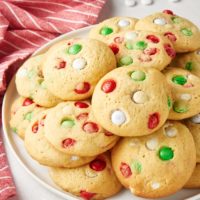 Christmas M&M Cookies piled on a white plate with M&Ms scattered around the plate