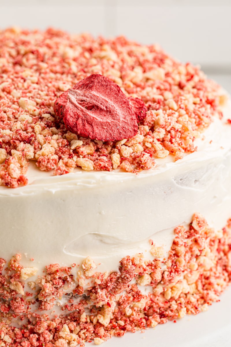 This crowd-pleasing strawberry crunch cake is made with real strawberries and rich cream cheese frosting, with crunchy cookie bits on top. Closeup of strawberry crunch cake with strawberry on top