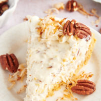 Slice of millionaire pie on plate with toasted coconut and pecans for garnish