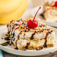 Slice of banana split cake topped with cherry and chocolate syrup