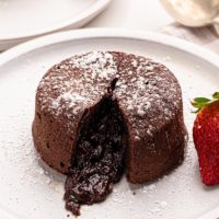 a chocolate lava cake on a white plate with the molten center oozing out of the cake