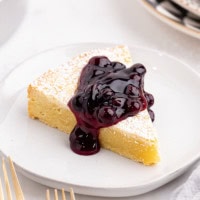 a slice of almond gâteau Breton topped with blueberry compote and served on a white plate